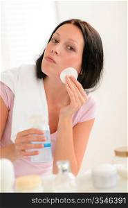 Young brunette woman face tonic cleaning with cotton pad bathroom