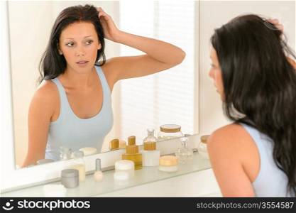 Young brunette woman in bathroom looking at herself in mirror