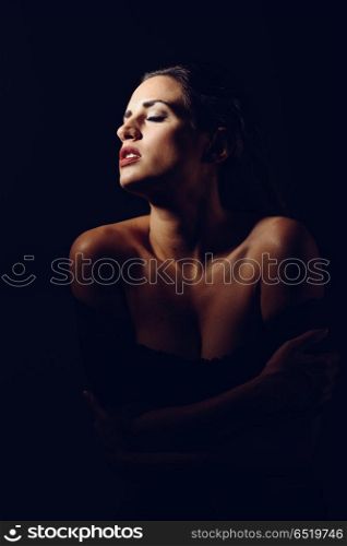 Young brunette woman in black lingerie in chiaroscuro lighting. Young brunette woman in black lingerie in chiaroscuro lighting. Attractive girl, model of fashion. Studio shot.