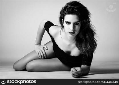 Young brunette woman in black lingerie lying on the floor. Attractive girl, model of fashion in black and white. Studio shot.