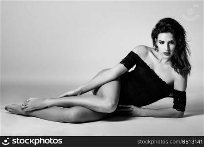 Young brunette woman in black lingerie lying on the floor. . Young brunette woman in black lingerie lying on the floor. Attractive girl, model of fashion in black and white. Studio shot.