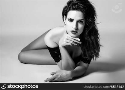 Young brunette woman in black lingerie lying on the floor. . Young brunette woman in black lingerie lying on the floor. Attractive girl, model of fashion in black and white. Studio shot.