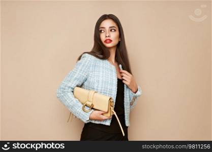 Young brunette woman in blue jacket. Model posing in a business suit. Girl  with beige handbag. Fashion photo