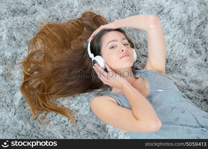young brunette woman listening music while laying on the carpet