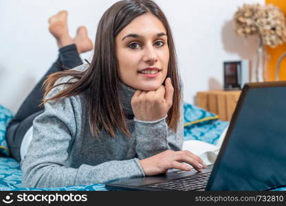 young brunette woman lying on the bed using a laptop