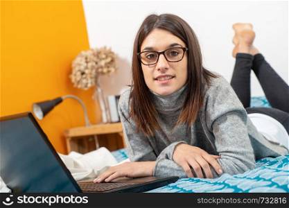 young brunette woman lying on the bed using a laptop