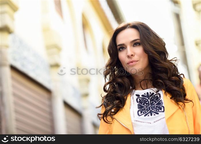 Young brunette woman, model of fashion, wearing orange modern jacket in urban background.