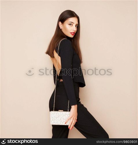 Young brunette woman posing in a black tight suit. Girl  with beige handbag. Brunette with long smooth and shiny hair. Fashion photo