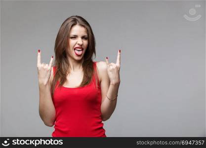 Young brunette woman showing rock and roll hand gesture posing in studio.. Young brunette woman showing rock and roll hand gesture posing in studio