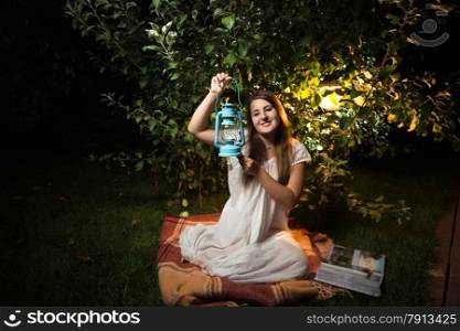 Young brunette woman sitting at garden at night and holding old lantern
