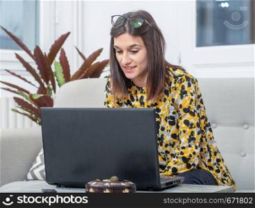 young brunette woman sitting in the couch using a laptop