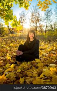 Young brunette woman sitting on grass at autumn park at sunny day