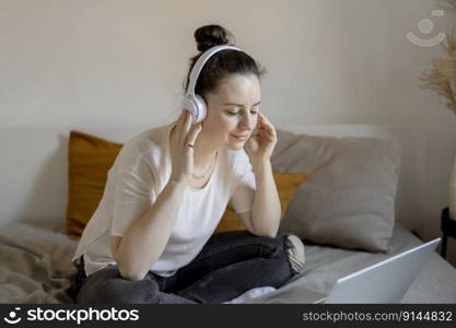 Young brunette woman sitting on the bed at home with casual clothes and listening music or audio book. Relaxing, resting. Time with yourself, mental health. Girl dreaming. Young brunette woman sitting on the bed at home with casual clothes and listening music or audio book. Relaxing, resting. Time with yourself, mental health. Girl dreaming.