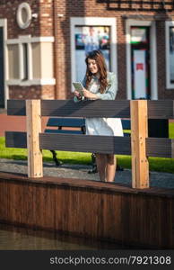 Young brunette woman standing on wooden bridge with tablet