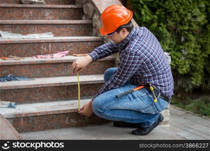 Young builder checking stairs height by measuring tape