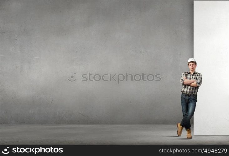 Young builder man leaning on white blank banner. Place for text. Builder with billboard