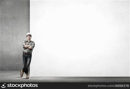 Young builder man leaning on white blank banner. Place for text. Builder with billboard