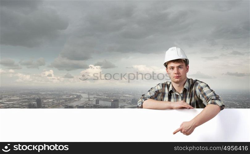 Young builder man with white blank banner. Place for text. Builder with billboard