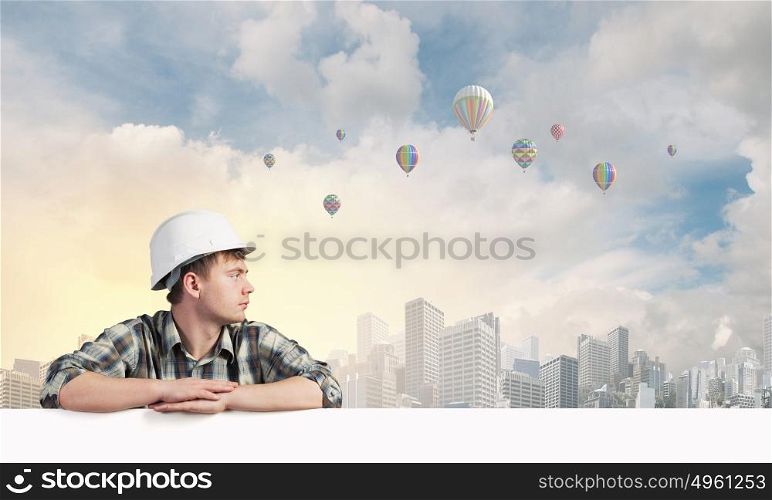 Young builder man with white blank banner. Place for text. Builder with billboard