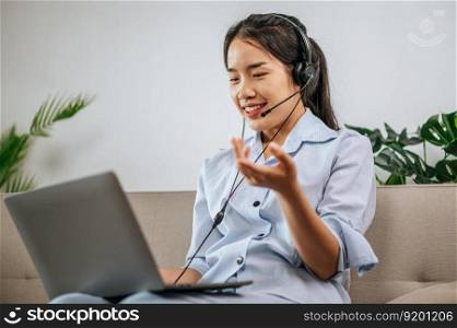 Young busi≠ss woman working on computer, talking onli≠using a headset whi≤sitting on the comfortab≤sofa at home. Concept of remote work from home