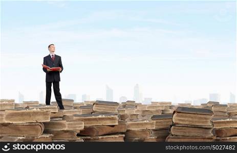 Young businesman standing on pile of old books. Man with red book