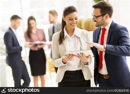Young business couple is working on a tablet while other young business people talking in the background