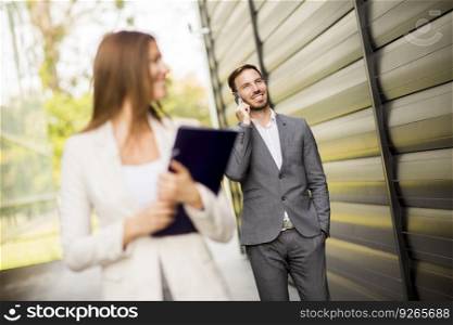 Young business couple walking and talking on the mobile phone outdoor. Focus on businessman