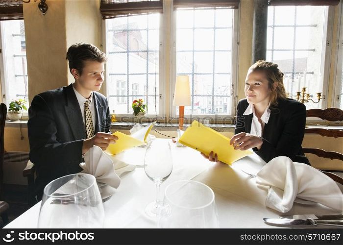 Young business couple with menus at restaurant table