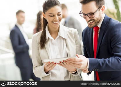 Young business couple working on tablet while other young business people talking in background