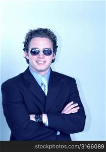 Young, business leader with sunglasses and dark blue suit is smiling and has his arms folded