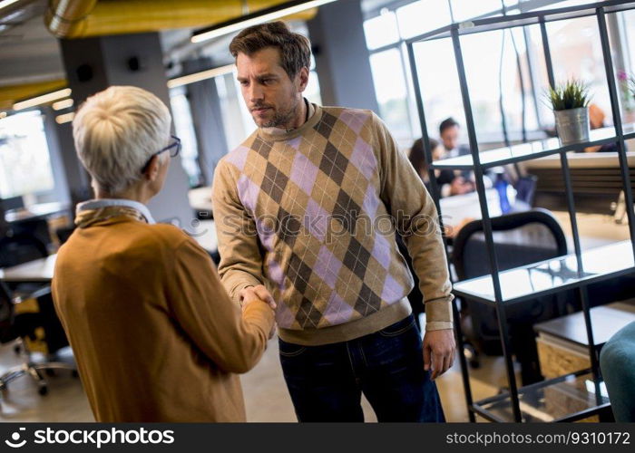 Young business man and senior business woman shaking hands in the modern office