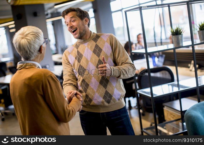 Young business man and senior business woman shaking hands in the modern office