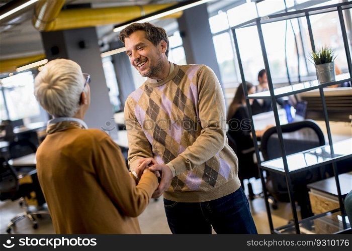 Young business man and senior business woman shaking hands in the modern office
