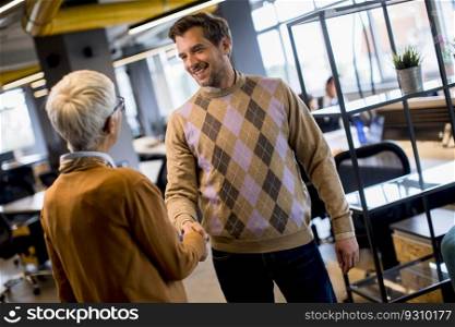 Young business man and senior business woman shaking hands in the modern office