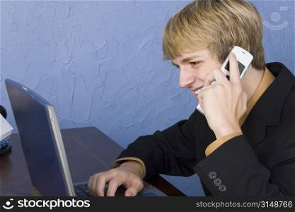 Young business man at desk speaking on cellphone.