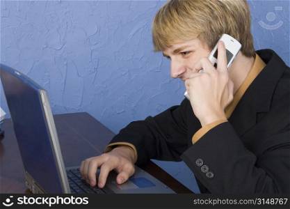 Young business man at desk speaking on cellphone.