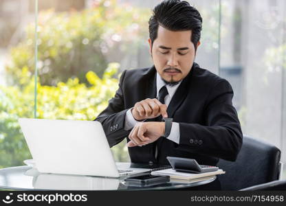 young business man checking time on smart watch while using laptop