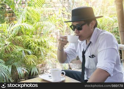 Young business man drinking coffee in garden at cafe