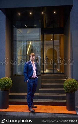 Young business man entering city hotel, looking for room, holding suitcases while walking on street