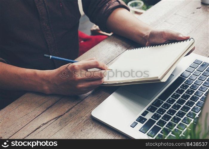 Young business man hand writing notebook and using laptop on wood table.