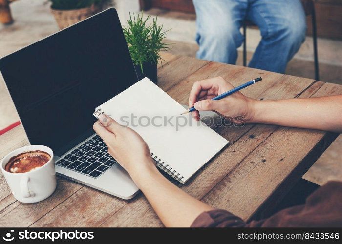 Young business man hand writing notebook and using laptop on wood table.