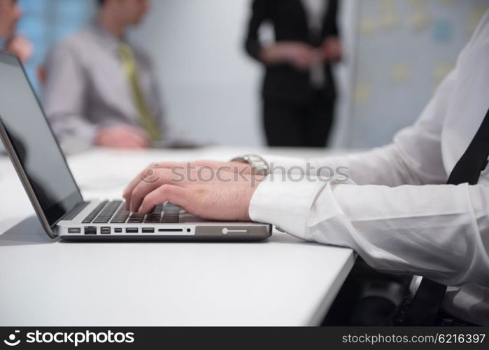 young business man hands typing on laptop computer on meeting, blured people group brainstorming in background at modern bright office interior