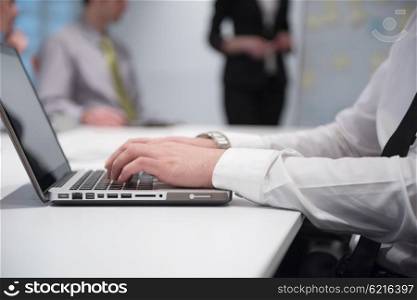 young business man hands typing on laptop computer on meeting, blured people group brainstorming in background at modern bright office interior