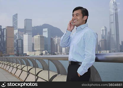 Young business man on bridge talking on mobile phone, smiling