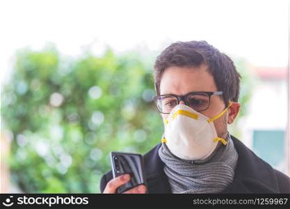 Young business man outdoors with a breathing mask and smartphone. Flue and corona season.