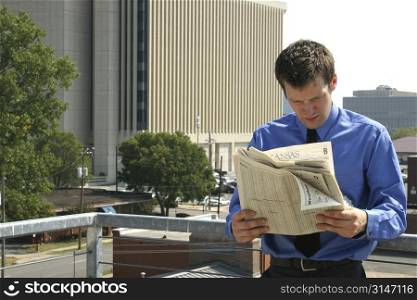 Young business man reading a newspaper with big city buildings in background. Shot with a Canon 20D.