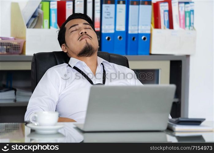 young business man sleeping on working desk between using laptop computer