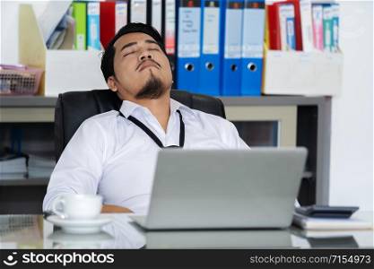 young business man sleeping on working desk between using laptop computer