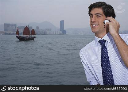 Young business man talking on mobile, traditional Chinese junk boat in background