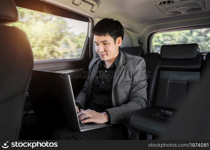 young business man using laptop computer while sitting in the back seat of car